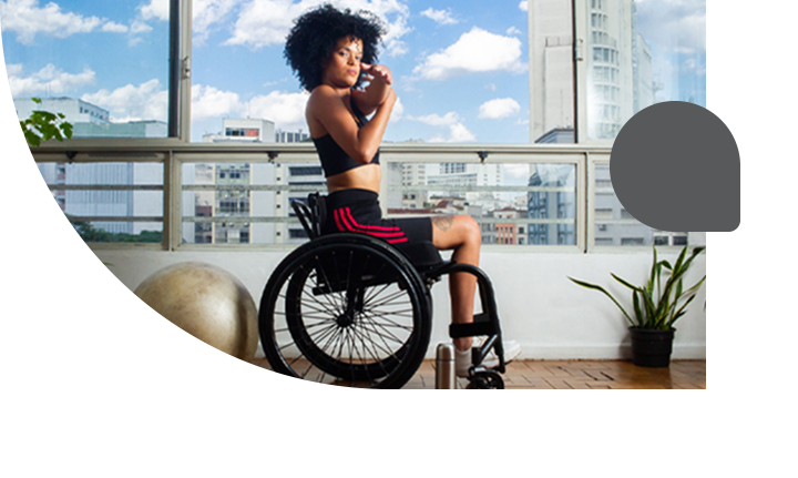 Mulher negra cadeirante, de cabelo black power, com roupas de academia, se exercitando.